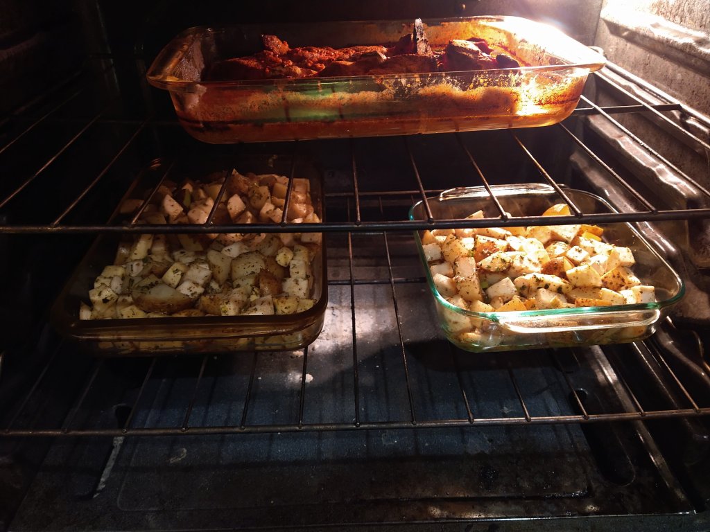 Picture of an oven with a pan of simmering Jerk Pork, and 2 other glass pans with chopped root vegetables. All roasting at 450 F