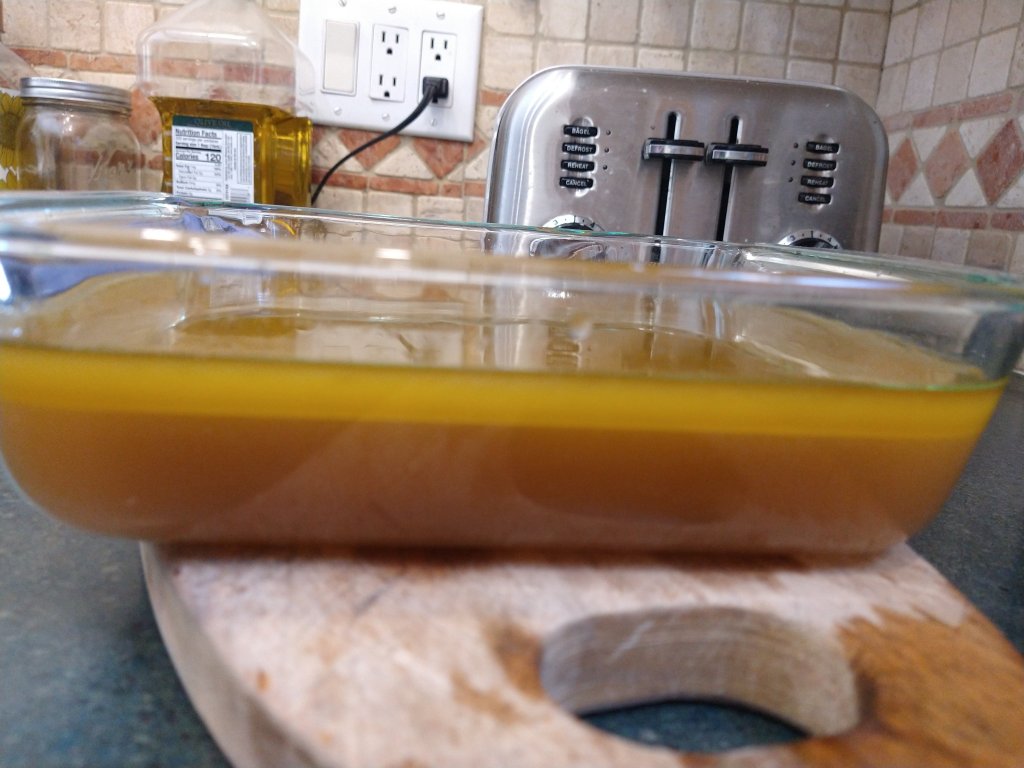 Side view photo of the strained cannabutter in a glass pyrex pan on my kitchen counter.