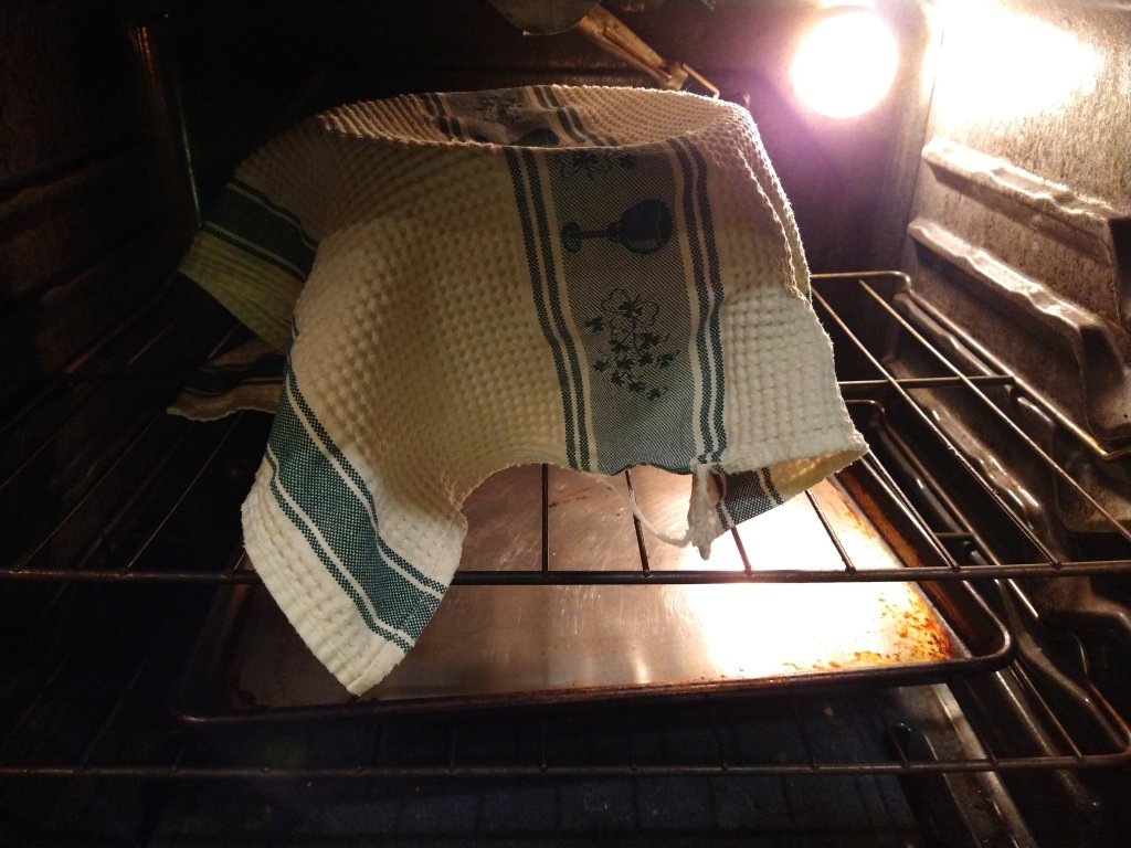 Picture of a kitchen aid bowl with rising cinnamon roll dough in a warm oven with a towel covering it.