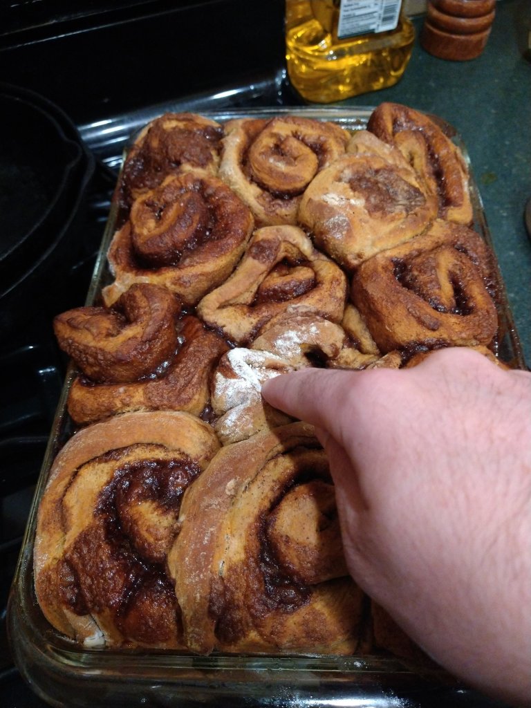 Picture of a hand poking the pumpkin spice cinnamon rolls for the baked texture. A quality check.