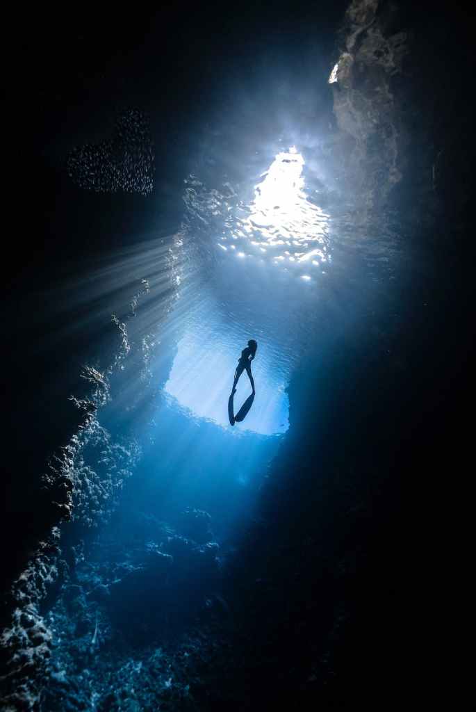 Woman underwater in an underground cave swimming towards the surface and light.