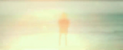 Man staring into the sunset ocean at a beach as the waves lap to him.