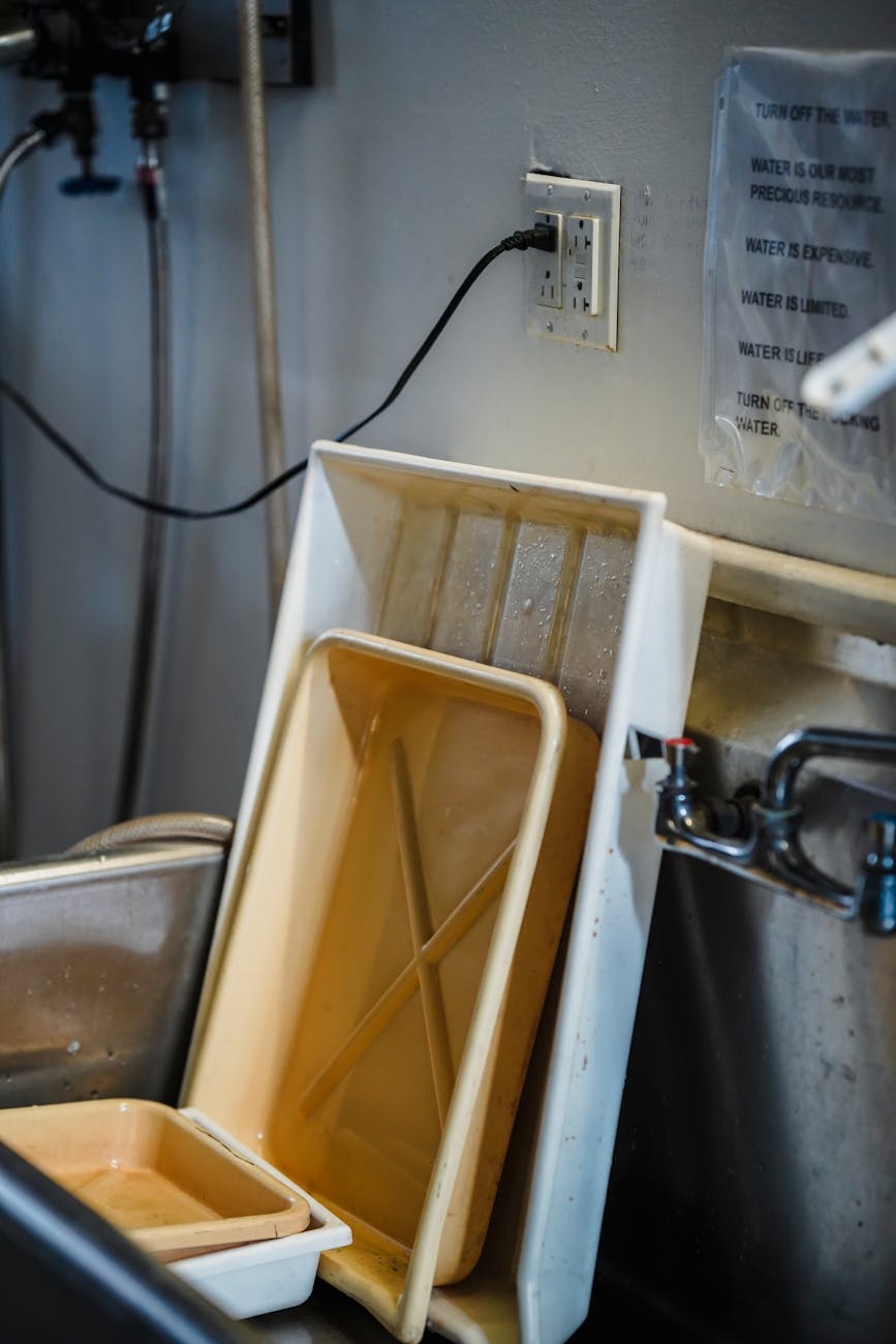 Picture of a professional style sink that you would find in a restaurant kitchen. In the picture there are a couple of plastic tubs or trays that are dirty and propped up diagonally.